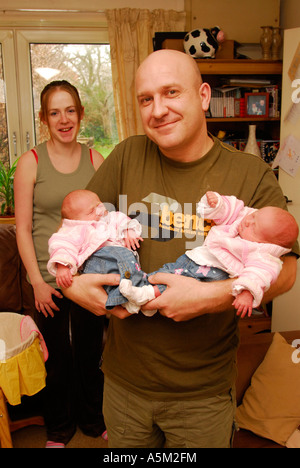 Stolzer Vater wiegt seine 10 Tage alten Zwillinge mit Ehefrau und Mutter im Hintergrund, Middlesex, UK. Stockfoto