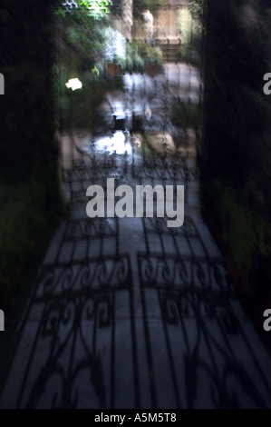 Ein Licht, das durch alte schmiedeeiserne Tore unheimliche Schatten im Innenhof eines Hauses im Garden District in New Orleans Louisiana Stockfoto