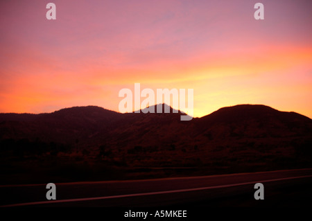 RAJ98901 Sonnenuntergang Himmel rot Orange rosa Leuchten mit Bergsilhouette Straße Stockfoto