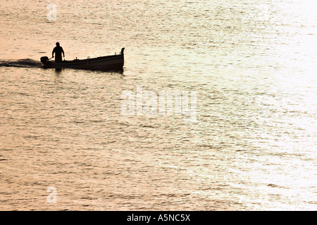 Gruß an die Sonne. Ein Fischer allein in einem kleinen offenen Boot umgeben von goldenen Kabbelwasser Erlöse aus im Morgengrauen Stockfoto