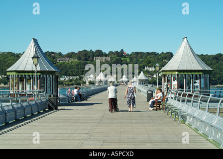 Ein paar Leute am Bangor Pier sitzen oder gehen an einem sonnigen Tag mit blauem Himmel in der Menai Strait und der Isle of Anglesey jenseits von Gwynedd North Wales UK Stockfoto