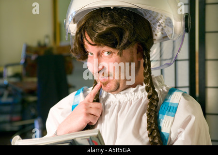 Mann, gekleidet wie eine Frau sitzt in einem Friseursalon unter Haartrockner Stockfoto