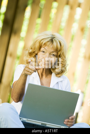 Ältere Frau mit Laptop, zeigt auf Kamera Stockfoto