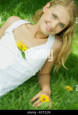 Frau liegend Gras mit Blume im Kleid, lächelnd in die Kamera Stockfoto