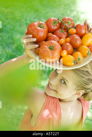 Junge Frau hält Schüssel Tomaten, lächelnd in die Kamera Stockfoto