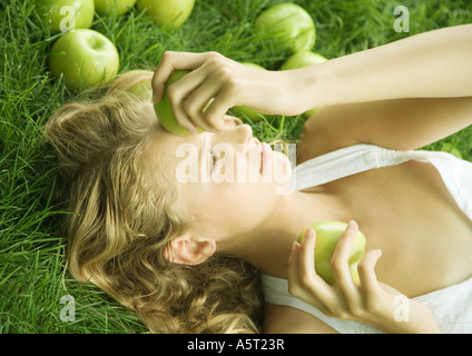 Frau liegend auf Rasen, hält Apfel auf Stirn Stockfoto