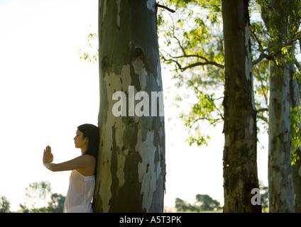 Frau stehend mit Hände im Gebet Position, Baum gelehnt Stockfoto