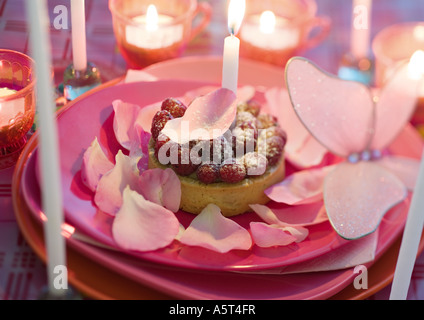 Himbeer Kuchen auf Teller mit Rosenblättern und Kerzen dekoriert Stockfoto