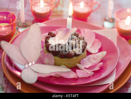 Himbeer Kuchen auf Teller mit Rosenblättern und Kerzen dekoriert Stockfoto