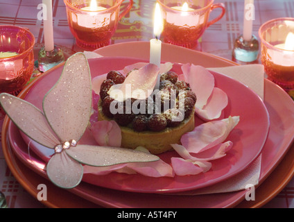 Himbeer Kuchen auf Teller mit Rosenblättern und Kerzen dekoriert Stockfoto