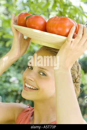 Frau Holding Schüssel voller Tomaten oben auf Kopf Stockfoto