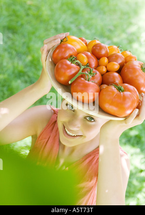 Frau Holding Schüssel voller Tomaten oben auf Kopf Stockfoto