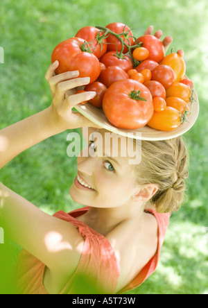 Frau Holding Schüssel voller Tomaten oben auf Kopf Stockfoto