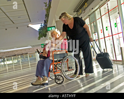 Ältere Frau im Rollstuhl mit Betreuer Begleiter im Abfertigungsbereich Flughafen prüft ihre Dokumente vor Antritt der Reise Stockfoto