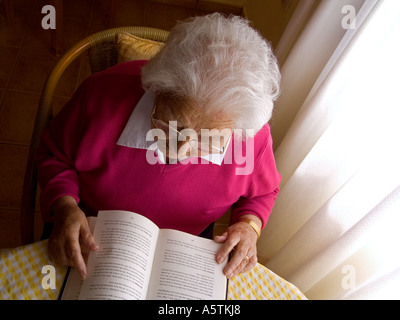 Ältere Dame Lesebuch am Wohnzimmertisch in natürliche Fensterlicht Stockfoto