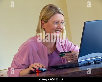 ONLINE SHOPPING KREDITKARTE DEBITKARTE lächelte zuversichtlich, Frau ihre Kreditkarte verwendet auf Linie mit ihren Laptop zu Hause shop Stockfoto