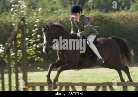 Junges Mädchen auf Pony springen Zaun im Springreiter Wettbewerb auf Land, UK Stockfoto