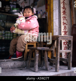 Junge, gut gekleidete Mädchen halten Kaninchen Kuscheltier sitzen in einem Geschäft, Yangshuo, Provinz Guangxi, China. Stockfoto