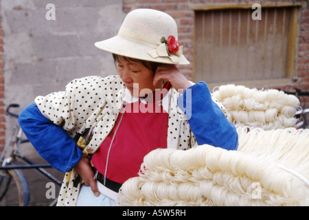 Naxi-Frau in traditioneller Kleidung und Strohhut wartet auf Kunden an ihrem Stand, Wase-Markt in der Nähe von Dali, Yunnan Provinz, China. Stockfoto