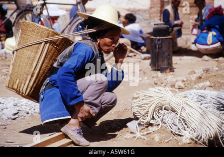 Einheimische Frau mit Korb auf dem Rücken, blaue Jacke, erwägt Kauf im Wase-Markt in der Nähe von Dali, Yunnan Province, China. Stockfoto