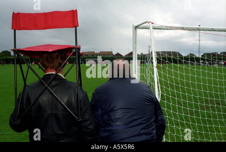 Fußball-Anhänger geht in Deckung vor dem Regen in ein FA-Cup-Unentschieden zwischen Diss Stadt und Suffolk Lokalrivalen AFC Sudbury. Stockfoto
