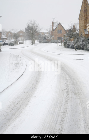 Auto-Spuren im Schnee auf einer leeren Straße führt in einer Wohnsiedlung in Market Harborough Leicestershire, England Stockfoto