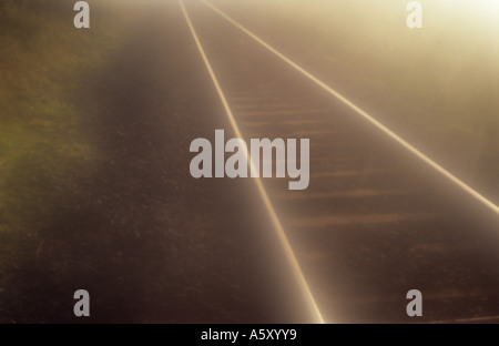 Stimmungsvollen Blick auf Eisenbahnschienen konvergieren in der Ferne in ein warmes goldenes Licht Stockfoto