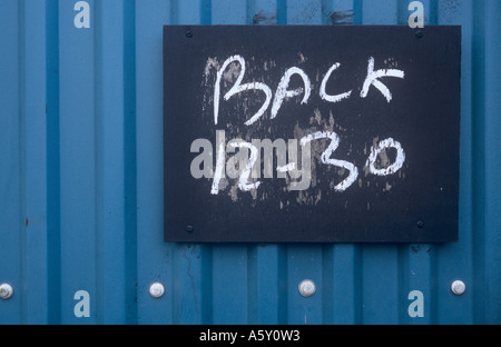 Getragen von Blackboard eine blaue Wellblech Zaun oder eine Mauer mit Wörter Kreide drauf besagt zurück 12.30 Uhr fixiert Stockfoto