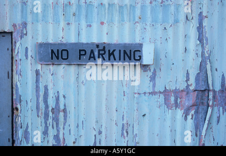 Detail einer zerkratzten verbeulte bemalten Wellblech-Wand mit einer Aluminium-Tür gesetzt und Hinweis erhalten keine Parkplätze Stockfoto