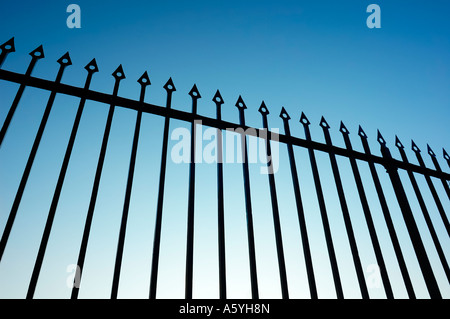 Ein Spike Metallzaun beschrieben gegen den blassen blauen wolkenlosen Abendhimmel Stockfoto