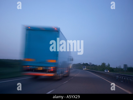 LKW GESCHWINDIGKEIT ENTLANG DER AUTOBAHN IN DER DÄMMERUNG UNTERWEGS Stockfoto