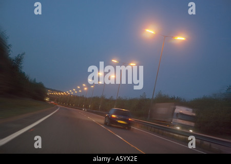 PKW- UND LKW-REISEN MIT GESCHWINDIGKEIT ENTLANG DER AUTOBAHN IN DER ABENDDÄMMERUNG Stockfoto