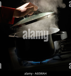 HAND HEBEN DECKEL SCHWENKEN VON KOCHENDEM WASSER UND STEIGT DAMPF SIEDEN AUF GASHERD Stockfoto