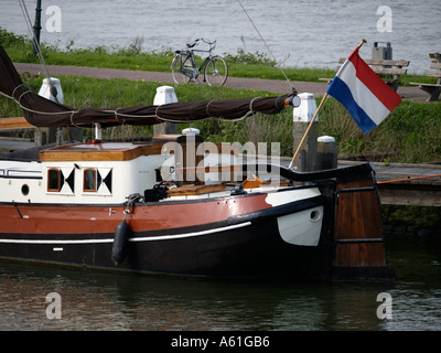 Heck des typischen niederländischen flachem Boden Segelschiff auf einem Deich in Woudrichem mit wehenden niederländischer Flagge und ein Fahrrad-Parken in der Nähe Stockfoto