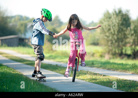 junges Mädchen, Einradfahren und ziehen ihren Bruder auf einem skateboard Stockfoto