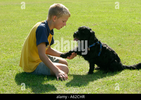 ein kleiner Junge neben seinem Hund auf einer Wiese hocken, ist sie Pfote geben. Stockfoto