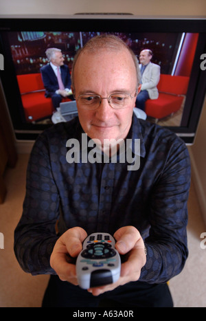EINE MITTE IM ALTER MANN MIT EINER FERNBEDIENUNG WÄHREND EINE NACHRICHTENSENDUNG IM FERNSEHEN UK ANGEZEIGT WIRD Stockfoto