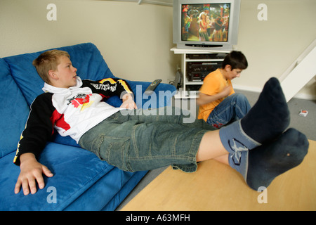 Porträt eines jungen Mannes geklebt, um das Fernsehen mit seinen Füßen auf dem Tisch Stockfoto