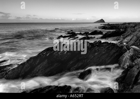 Monochrome dawn Licht an wembury Strand mit dem Meer wirbeln um die freiliegende Felsen und die mew Stein am Horizont Stockfoto