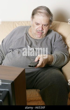 Couch-Potato. Übergewichtiger Mann nutzt Fernbedienung, um TV-Kanäle zu ändern. Stockfoto