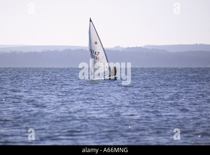 Einsamer Mann Segeln einen kleinen ein-Mann-Segelboot auf dem Solent Wasser gebadet in Early Frühlingssonne von Stokes Bay, Gosport, Engl Stockfoto