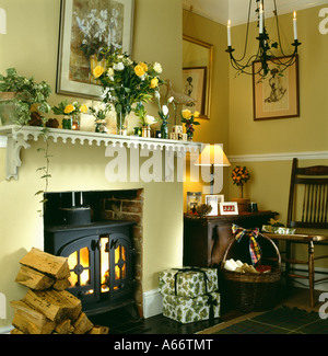 Beleuchtete gusseiserne Ofen Kamin mit Haufen von Protokollen und verpackte Geschenke im traditionellen Wohnzimmer mit beleuchteten Lampe auf Tisch Stockfoto