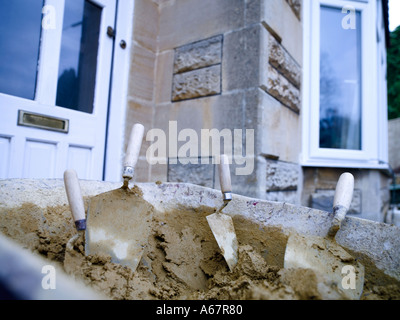 Schubkarre vor Haus voll von Zement mit vier Trowls Stockfoto