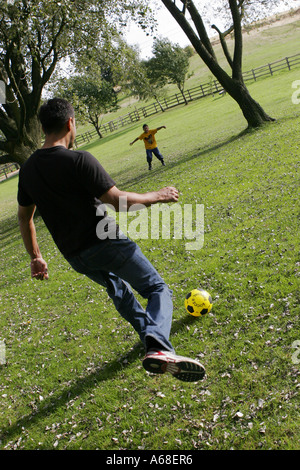 Asian-Vater und Sohn Fußball spielen in der englischen Landschaft Stockfoto