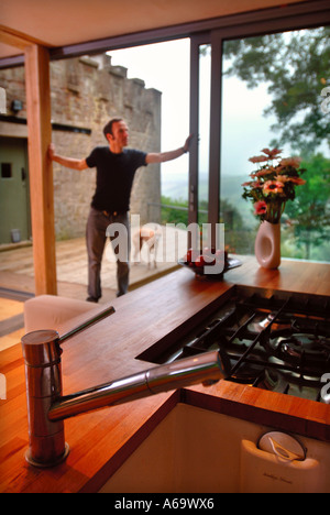 EIN MANN ÖFFNET DIE GLAS-SCHIEBETÜREN VON EINEM MODERNEN HAUS UK Stockfoto