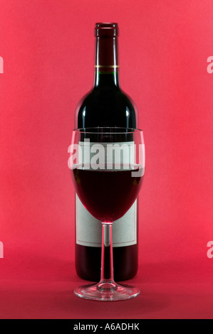 Glas Rotwein und eine Flasche auf einem roten Hintergrund Stockfoto