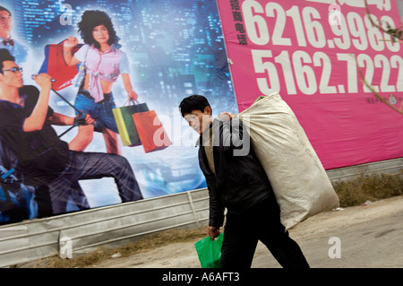 Wanderarbeitnehmer mit seinem Gepäck geht vorbei an einer Plakatwand mit China' s modernen Lebens für eine Gewerbeimmobilie in Peking 2006 Stockfoto