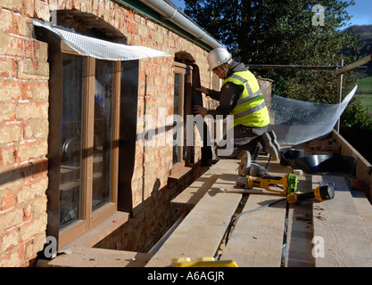 EINBAU EINER SCHÜTZENDEN FEUCHTEN BEWEIS KUNSTSTOFF MEMBRAN WÄHREND DER BEFESTIGUNG NEUE HARTHOLZ FLÜGELFENSTER AUF EINER HÜTTE UNTER RENOVIERUNG UK Stockfoto