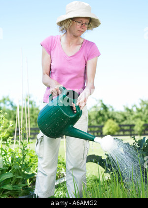 junge Frau mit Hut an einem heißen Sommertag mit Wasser aus einem Sprinklerkopf auf einer Garten Gießkanne Stockfoto