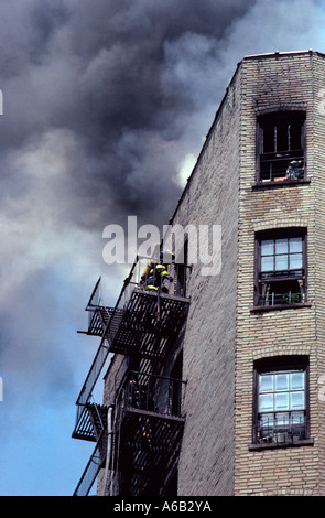 Feuerwehrmänner betreten ein brennendes Wohngebäude über eine Feuertreppe. Feuerwehrleute klettern Treppen, um das rauchgefüllte Mietshaus zu betreten. Die Bronx New York Stockfoto